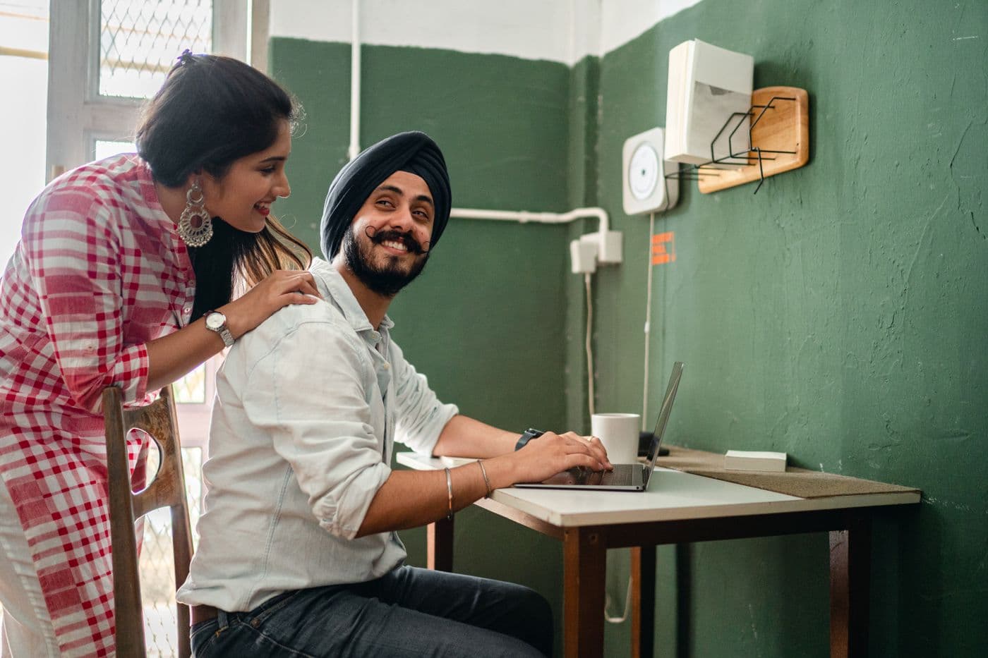 A man working on his laptop at home while his partner leans in, both smiling